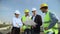 Construction engineer holding architectural plan explaining to workers helmets