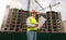 Construction engineer in safety vest and helmet posing aginst working cranes and buildings