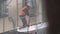 Construction laborer in orange uniform vest scratches wall with hammer on scaffolding