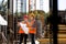 Construction manager and engineer dressed in orange work vests and hard helmets explore construction documentation on