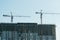 The construction of a multi-storey building. In the frame high-rise cranes and people. Monolithic building encased in