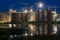 Construction of multi-storey modern houses with cranes at night near the pond with reflected lights