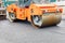 Construction of a new road. A large vibratory road roller paired with an asphalt paver paving and compacting the hot asphalt on