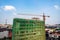 Construction site next to modern office, residential building. Working crane and safety net with cloud blue sky . Green grid