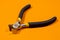 The construction tool ticks pliers metal steel with a black handle on an orange background. For snacking wire, small size