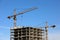 Construction tower cranes above unfinished residential building on blue sky background