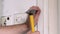 Construction worker and handyman with yellow hammer strikes and nails a nail into wooden wall of kitchen door at construction site