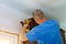 Construction worker nailing brad nail air gun to crown moulding on white kitchen cabinets