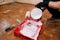 Construction worker and painter with black gloves pours white color from bucket into red bowl for paint mixing.