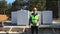 A construction worker in a protective yellow helmet and a signal vest stands in front of the construction site of a house with a f