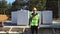 A construction worker in a protective yellow helmet and a signal vest stands in front of the construction site of a house with a f