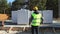 A construction worker in a protective yellow helmet and a signal vest stands in front of the construction site of a house with a f