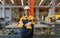 A construction worker stand in front of a bustling factory. He\\\'s sporting a hard hat and safety vest