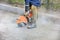 A construction worker using a portable gasoline saw cuts old asphalt to repair a site on the road