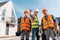 Constructors in helmets holding toolboxes near coworker gesturing