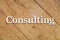 `Consulting` white text on a wooden background.