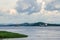 Container cargo ships on mighty Congo river with dramatic cloudy sky and lush green grass in foreground, DRC, Africa