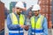 Container operator wearing white helmet and reflection shirt and holding tablet doing routine inspection while working in