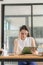 Contemplative Asian female executive in shirt working with laptop in modern office