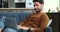 Contemplative Man on Living Room Sofa Typing on Laptop with a Smile