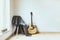 Contemporary home interior. Black chair covered with woolen gray blanket and acoustic guitar in front of an empty white wall.