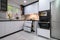 A contemporary kitchen with white cabinets, a marble floor, an open oven door, and pull-out shelves