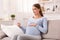 Content Pregnant Woman Using Digital Tablet Reading At Home