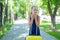 A contented little girl in a blue dress is standing alone in the street with a yellow suitcase and waiting for her