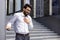 Contorted in pain, a young Indian male businessman stands by the wall of an office building and holds his hand over his