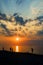 Contours of people walking by the sea at sunset against the backdrop of dramatic clouds