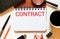 CONTRACT. The word CONTRACT is written on a light notebook near glasses, a calculator on a wooden background