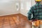 Contractor Wearing Toolbelt and Hard Hat Facing Empty Room with Hard Wood Floors