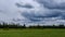 Contrast rain storm clouds over green meadow and some trees in summer. blue sky before the rain