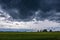 Contrast rain storm clouds over green meadow and some trees in summer. blue sky before the rain