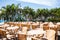 Contrast view of open-air cafe with tables and chairs and background of palms