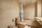 Conventional bathroom with marble top, frameless mirror embedded in cream marble wall, brown porcelain bathtub with handles and