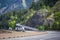 Convoy of the big rig semi trucks with different semi trailers running on the turning divided road along the rocky mountain ranges