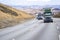 Convoy of big rigs semi trucks with loaded semi trailers hard climbing uphill on the winding highway road to mountain pass