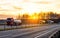 A convoy of three trucks transports dangerous goods in tank semi-trailers on a motorway against the backdrop of sunset in the