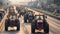 A convoy of tractors driving in a line on a highway during a peaceful protest, with a crowd of supporters and a setting