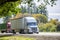 Convoy of two different big rigs semi trucks with dry van and container semi trailers running on the summer road with green trees