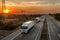 Convoy of white lorry trucks on a highway at sunset