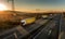 Convoy of white transportation trucks with yellow trailers in line on a country highway at sunset