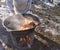 A cook in an apron prepares food on the street in a cauldron on a fire. A man cooks rice with meat.