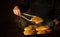 The cook bakes hot dog buns. Tongs in chef hand and baking sheet with hot pies. Place for advertising on a dark background