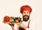 Cook with cheerful face in burgundy uniform holds salad ingredients. Chef holds board with fresh vegetables. Cooking and