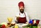 Cook with cheerful face in burgundy uniform sits by table