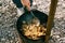 The cook cooks pilaf in the cauldron on an open fire outside, stirring with a large ladle.