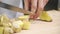 Cook cuts into cubs ginger on wooden board inside industrial kitchen