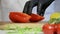 A cook cuts a red pepper in half with a knife on a chopping Board, slow motion.
